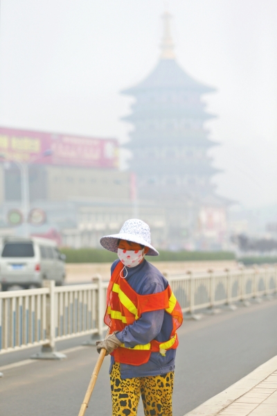 近日，在古都洛陽(yáng)，環(huán)衛(wèi)工人身后的“天堂”被霧霾籠罩著。