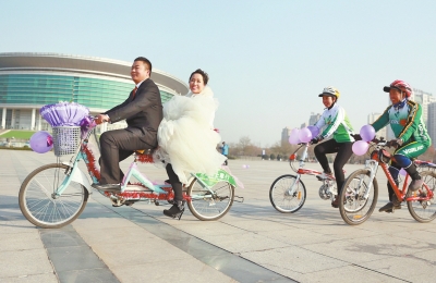 氣球和鮮花裝點(diǎn)的雙人自行車，新郎郝幸福載著美麗新娘回家。