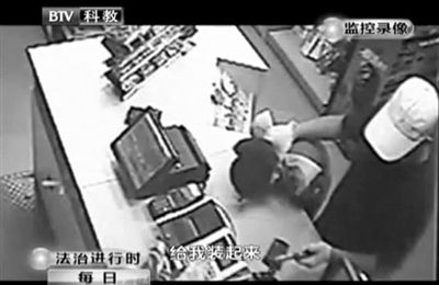 戴帽男子一手掐住加油站營業(yè)員，一手持發(fā)令槍指向另一營業(yè)員，要求“把錢給我裝起來”。