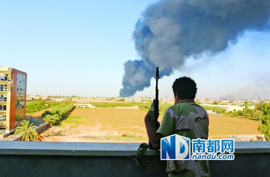 2日，利比亞首都的黎波里，一民兵武裝成員眺望被火箭彈擊中的儲油罐冒出濃煙。