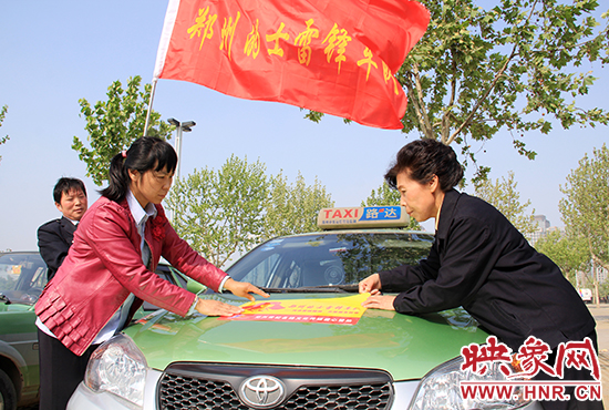 　　授旗結(jié)束后，首都的士雷鋒車隊(duì)王鳳進(jìn)隊(duì)長(zhǎng)（右）與鄭州的的哥的姐在車身上貼上標(biāo)識(shí)。