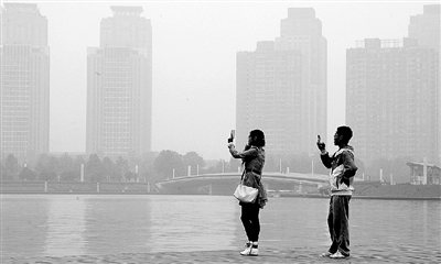 29日中午，鄭東新區(qū)如意湖畔，兩個年輕人拍攝霧霾中的景色。 鄭州晚報記者 馬健 圖