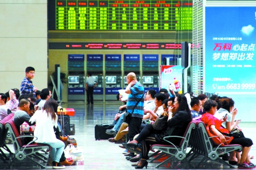 候車大廳溫度很高，一名乘客一手扇風(fēng)、一手擦汗