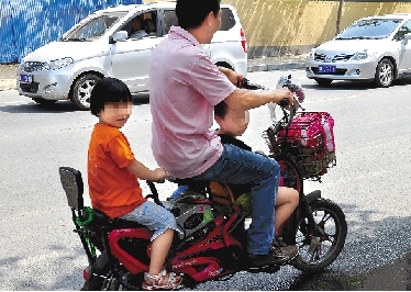 周先生騎著一輛低矮的電動車帶著一對兒女，很不安全。