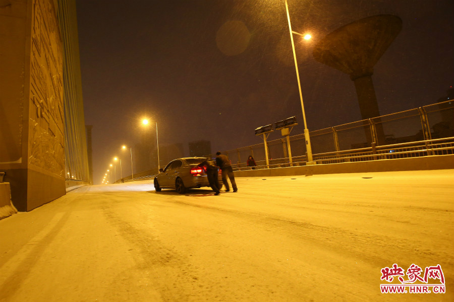 雪天路滑，汽車上橋打滑，兩名“推車人”幫助一輛私家車上坡。