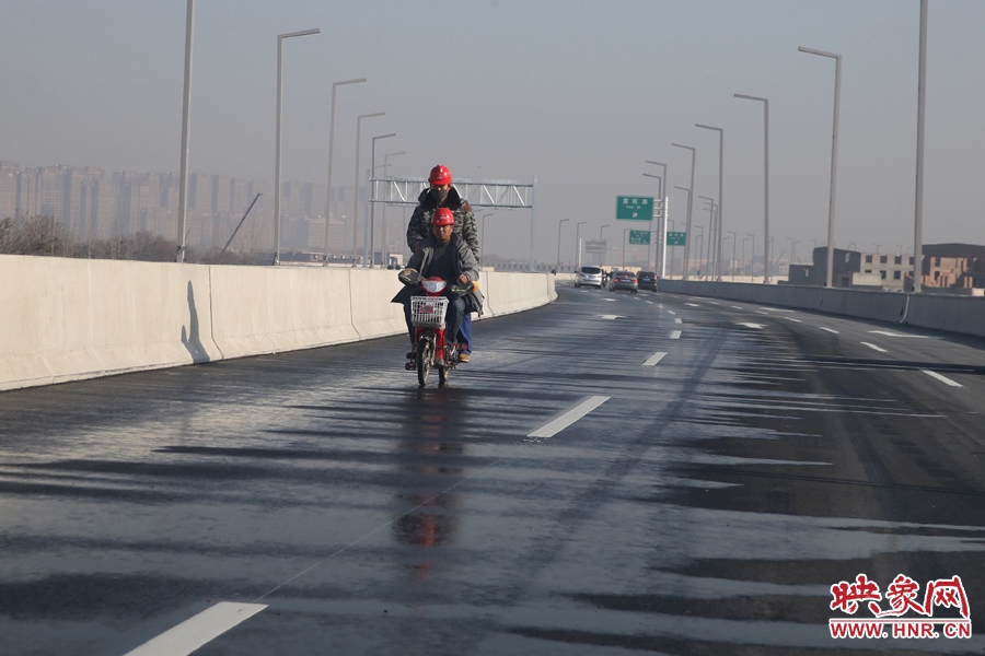 兩名工人騎車經(jīng)過灑水養(yǎng)護路面。