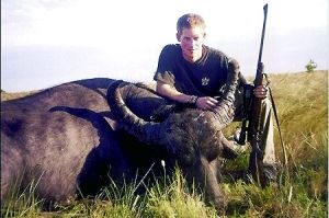 哈里王子手持獵槍，蹲在一頭遭到獵殺的水牛旁邊