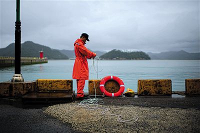 7月6日，韓國(guó)珍島，一名海岸警察在港口系救生圈。4月，客輪在珍島近海發(fā)生沉船事故后，仍有11人下落不明。