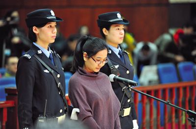 被告人盧梅低著頭，站在朝陽法院刑事審判庭的被告席上。