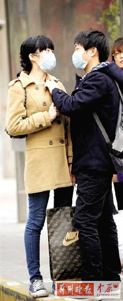 公交站臺上，一對年輕人戴著口罩，系緊衣領(lǐng)。